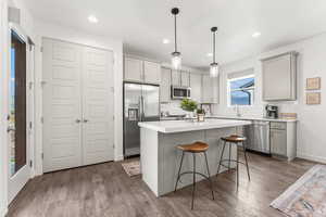 Kitchen with appliances with stainless steel finishes, dark wood-type flooring, a kitchen bar, and gray cabinetry