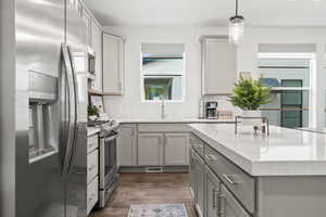 Kitchen featuring dark wood-style flooring, stainless steel appliances, gray cabinets, decorative backsplash, and a sink