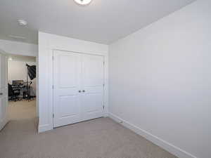 Unfurnished bedroom with a closet, light carpet, visible vents, and baseboards