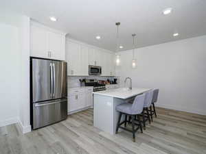 Kitchen with a breakfast bar area, stainless steel appliances, tasteful backsplash, white cabinets, and a sink