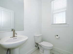 Half bath with marble finish floor, a sink, toilet, and baseboards