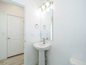 Half bathroom featuring toilet, a sink, baseboards, and wood finished floors