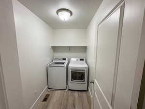 Clothes washing area featuring laundry area, visible vents, light wood-style flooring, a textured ceiling, and washing machine and dryer