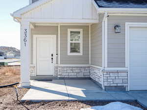 Doorway to property with a garage, stone siding, a shingled roof, and board and batten siding