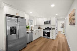 Kitchen featuring appliances with stainless steel finishes, white cabinets, a sink, and light countertops