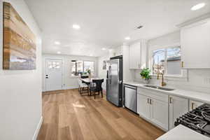 Kitchen featuring stainless steel appliances, a sink, white cabinets, light countertops, and light wood-type flooring