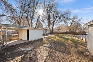 View of yard with a carport, an outbuilding, and fence