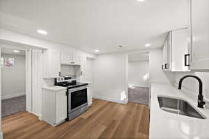 Kitchen with electric stove, a sink, light wood-style flooring, and white cabinets