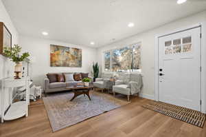 Living area with light wood finished floors, baseboards, a textured ceiling, and recessed lighting