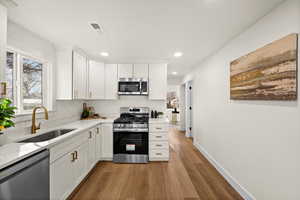 Kitchen with stainless steel appliances, visible vents, light wood-style flooring, white cabinets, and a sink