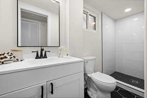 Bathroom featuring toilet, recessed lighting, a tile shower, and vanity