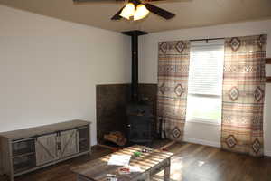 Living room with a wood stove, dark wood-style flooring, ceiling fan, and baseboards