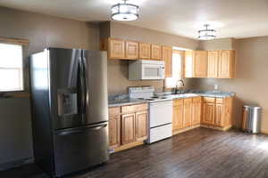 Kitchen with white appliances, light brown cabinets, a sink, and dark wood-style flooring