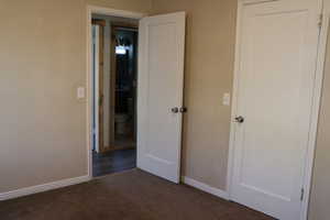 Unfurnished bedroom with dark carpet and baseboards