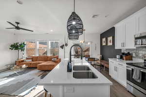 Kitchen featuring stainless steel appliances, wood finished floors, a sink, visible vents, and an island with sink