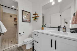 Full bathroom featuring baseboards, a tile shower, vanity, and toilet