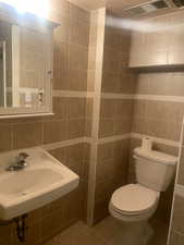 Half bathroom featuring visible vents, a sink, toilet, and tile walls