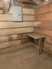 Unfinished basement featuring wood walls and electric panel