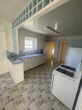 Kitchen with white gas range, a sink, light countertops, backsplash, and white cabinetry