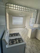 Kitchen with visible vents, white range with gas cooktop, a ceiling fan, light countertops, and brick patterned floor