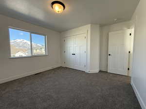 Unfurnished bedroom with a textured ceiling, visible vents, baseboards, a closet, and dark carpet