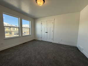 Unfurnished bedroom with baseboards, visible vents, dark carpet, and a textured ceiling