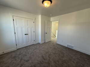 Unfurnished bedroom featuring baseboards, visible vents, and dark carpet