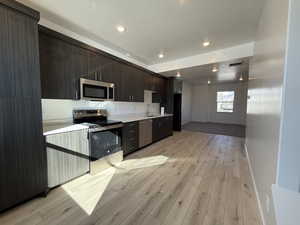 Kitchen with light countertops, appliances with stainless steel finishes, light wood-style floors, a sink, and dark brown cabinetry