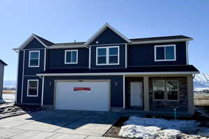 Traditional-style home featuring an attached garage, covered porch, concrete driveway, stone siding, and board and batten siding