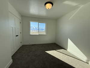 Unfurnished room featuring a textured ceiling, dark carpet, visible vents, and baseboards