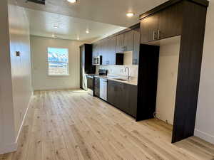 Kitchen with stainless steel appliances, a sink, dark brown cabinets, light countertops, and light wood-type flooring