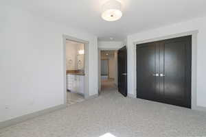 Unfurnished bedroom featuring a closet, light colored carpet, baseboards, and ensuite bath