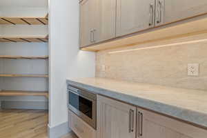 Kitchen featuring stainless steel microwave, light countertops, light brown cabinetry, light wood-style floors, and backsplash