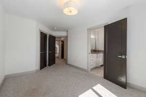 Unfurnished bedroom featuring baseboards, ensuite bathroom, and light colored carpet