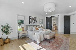 Bedroom featuring recessed lighting, light wood-style flooring, a barn door, connected bathroom, and baseboards