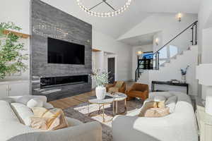 Living room with lofted ceiling, a fireplace, wood finished floors, stairway, and an inviting chandelier