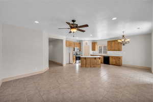 Kitchen with baseboards, a kitchen island, stainless steel appliances, light countertops, and ceiling fan with notable chandelier