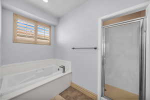 Bathroom featuring a stall shower, a garden tub, and baseboards