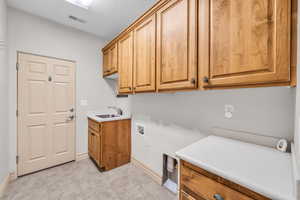 Clothes washing area featuring hookup for a washing machine, visible vents, cabinet space, a sink, and a textured ceiling