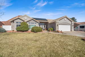 View of front of property featuring concrete driveway, an attached garage, fence, roof mounted solar panels, and a front yard