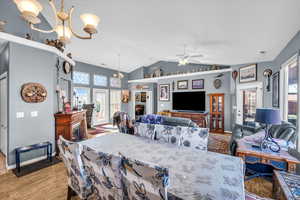 Dining room with vaulted ceiling, ceiling fan with notable chandelier, baseboards, and light wood-style floors