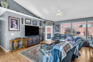 Living room featuring a ceiling fan, vaulted ceiling, baseboards, and wood finished floors