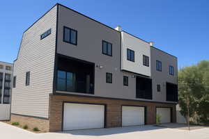 Back of property with an attached garage, driveway, brick siding, and a balcony