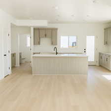 Kitchen with light wood finished floors, a kitchen island with sink, and light stone countertops