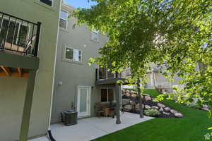 Rear view of property featuring a patio, central AC unit, a balcony, a lawn, and stucco siding