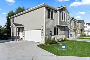 View of front of house featuring concrete driveway, stone siding, an attached garage, a front lawn, and stucco siding