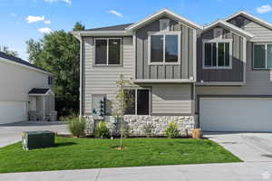 View of front facade with driveway, board and batten siding, and stone siding