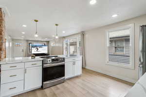 Kitchen with recessed lighting, stainless steel appliances, white cabinetry, light wood-style floors, and hanging light fixtures