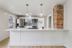 Kitchen featuring a peninsula, hanging light fixtures, appliances with stainless steel finishes, light stone countertops, and tasteful backsplash