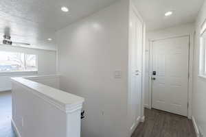 Hallway featuring stairs landing, wood finished floors, a textured ceiling, baseboards, and recessed lighting